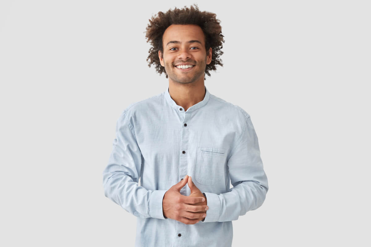 attractive mixed race male with positive smile shows white teeth keeps hands stomach being high spirit wears white shirt rejoices positive moments life people emotions concept