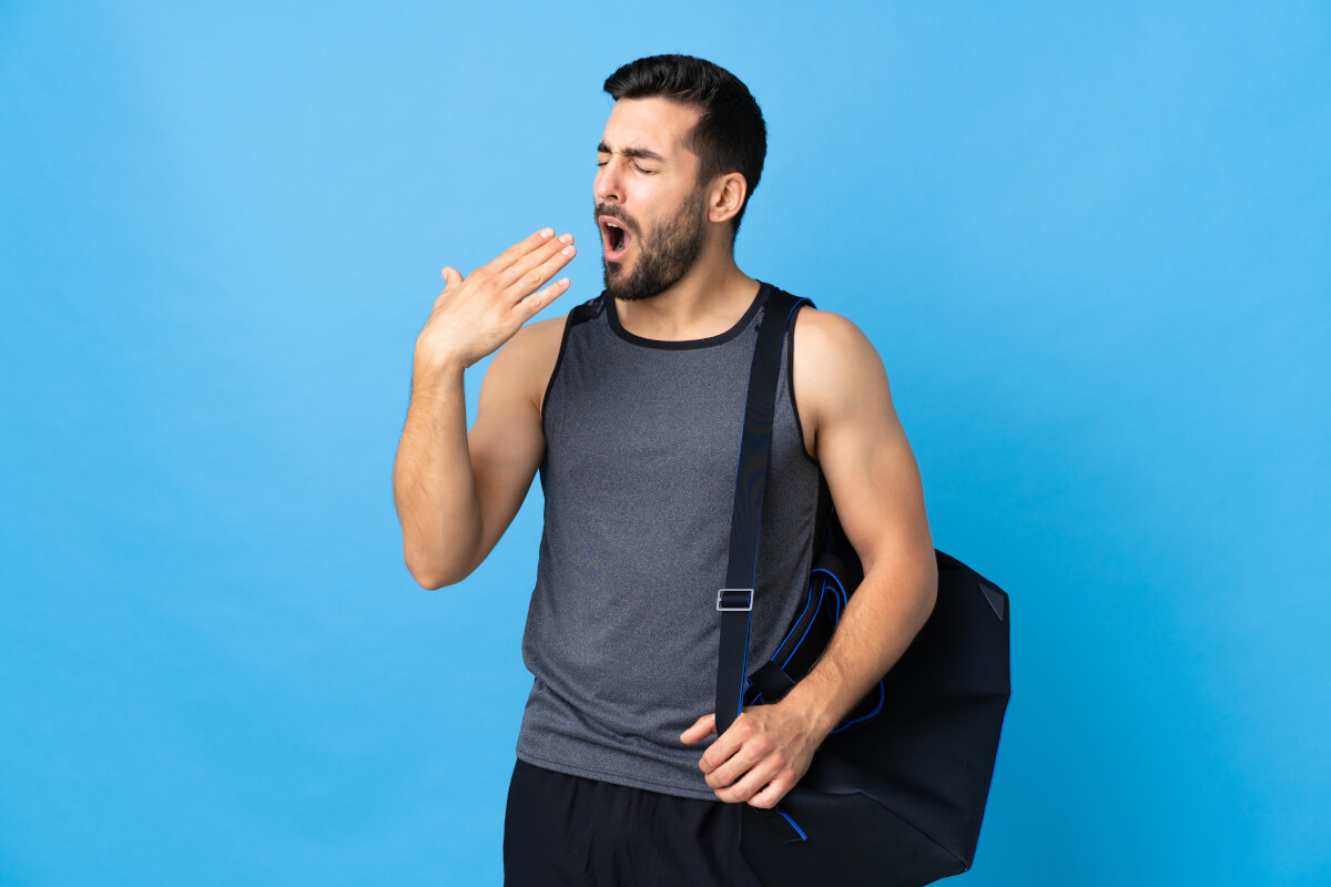 young sport man with sport bag isolated blue background yawning covering wide open mouth with hand