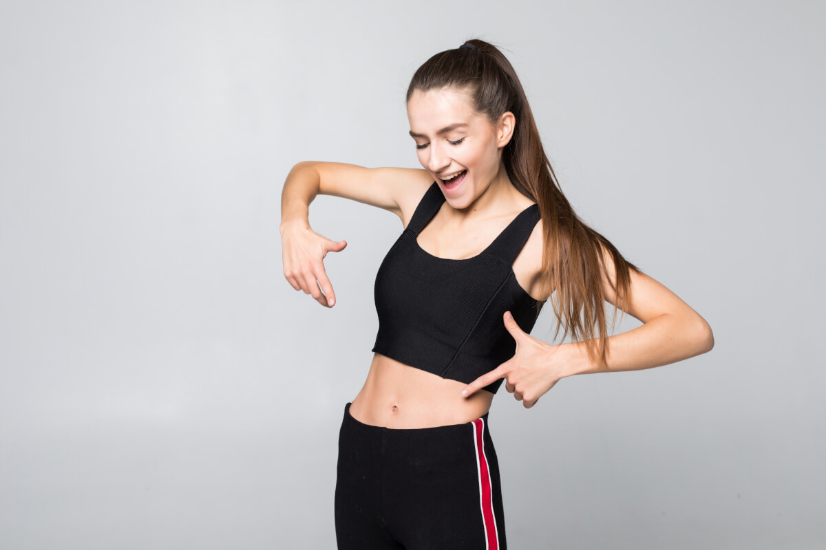 fitness exercise diet concept portrait woman pointing finger her six pack isolated white wall