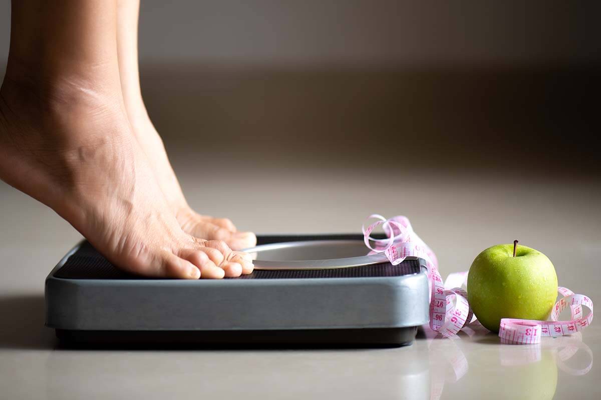 female leg stepping weigh scales with measuring tape apple